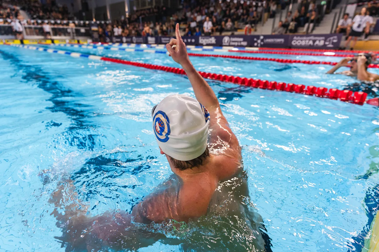 Daniel celebrating in the pool with an arm raised toward the crowd.