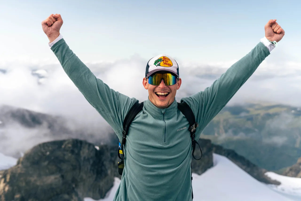 Daniel with his arms raised on a snowy mountain summit.